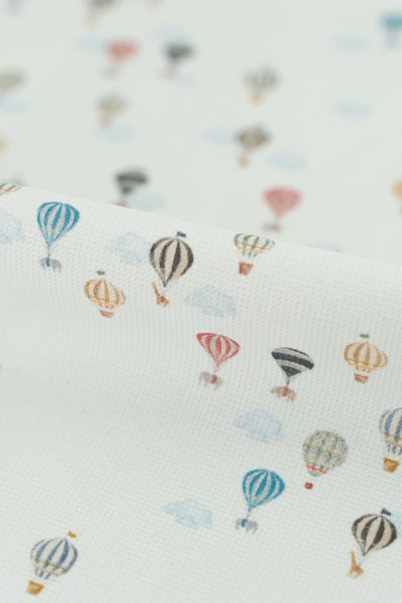 Tejido con estampaod infantil de globos aerostáticos y nubes en tonos suaves y pastel.