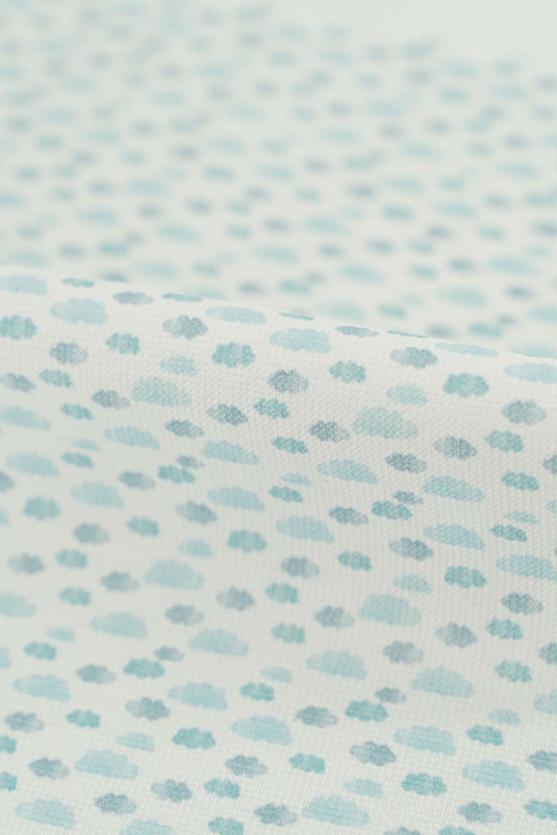 Tejido con estampado infantil de nubes en tonos azules suaves y pastel. 