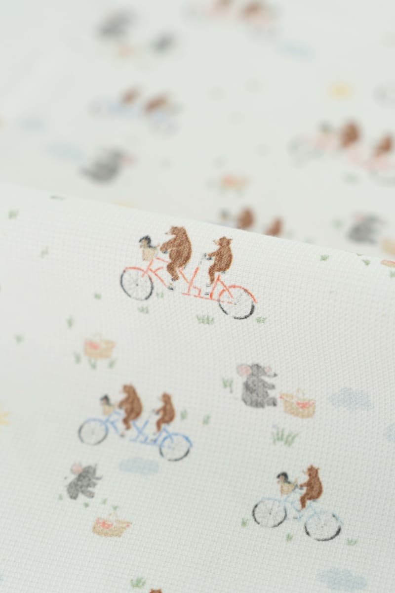 Tejido con estampado infantil de osos montando en bicicleta y lefantes de picnic.