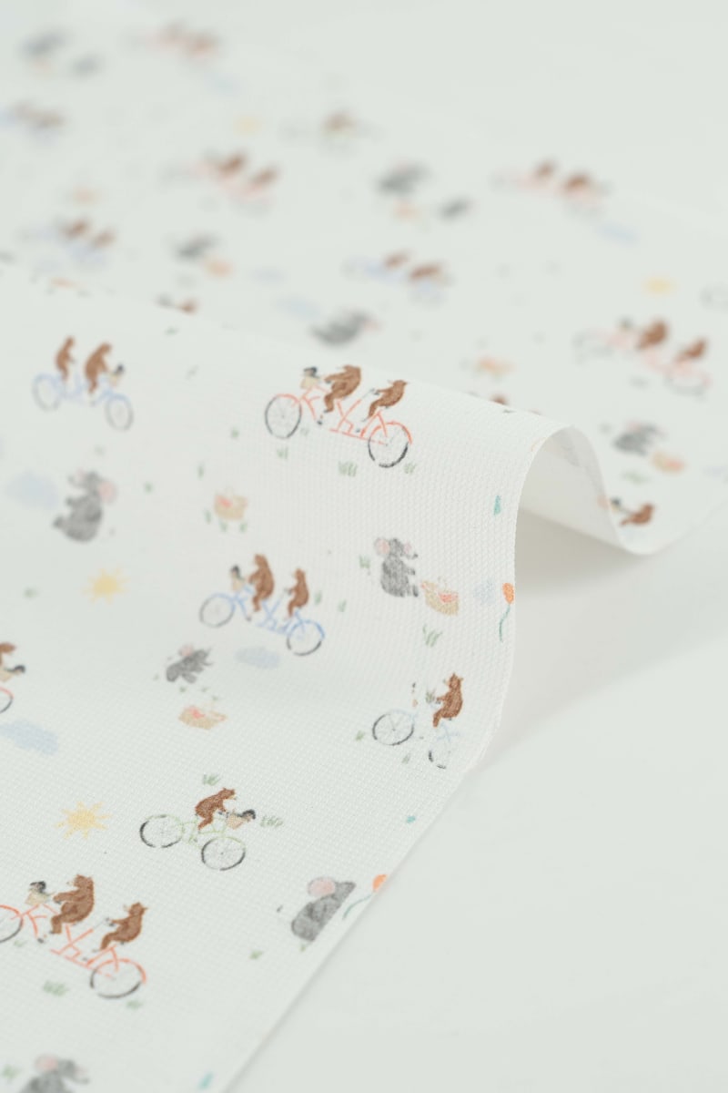 Tejido con estampado infantil de osos montando en bicicleta y lefantes de picnic.