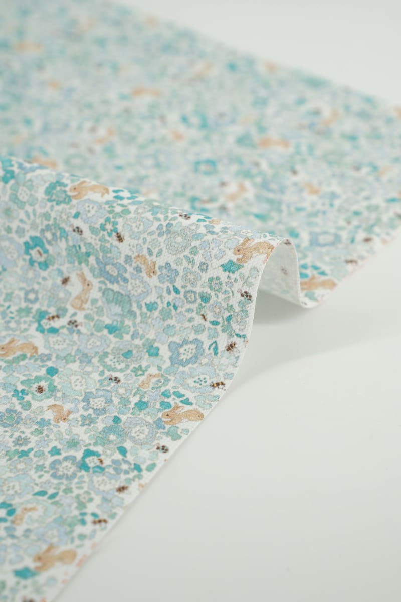 Tejido infantil con estampado de flores y conejos. En tonos azules y patel. 